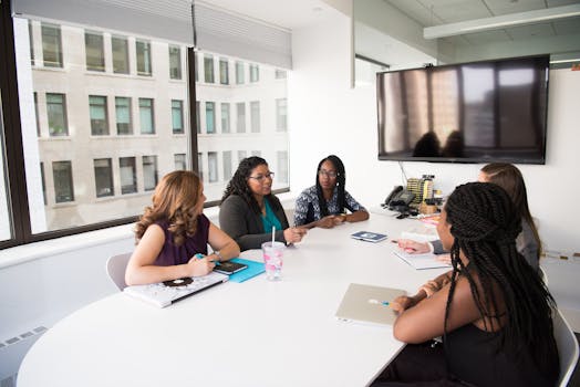 A group of diverse women engage in a business discussion in a modern office setting.