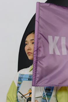 A woman in stylish clothing holds a purple flag indoors, conveying individuality.