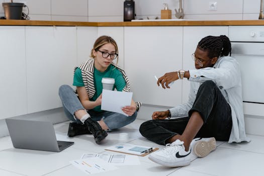 Young professionals in casual clothing brainstorming on the kitchen floor with documents and a laptop.